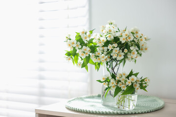 Bouquet of beautiful jasmine flowers in vase on table indoors. Space for text