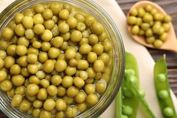 Pickled peas in jar and pods on wooden table, flat lay