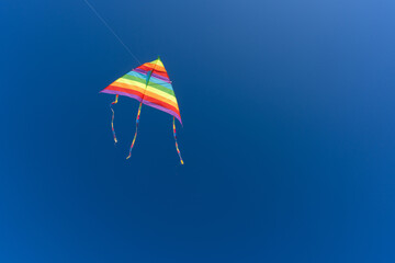 Close-up of a vibrant rainbow kite soaring in the clear blue sky on a sunny day, symbolizing freedom, fun, and childhood joy during a beach adventure