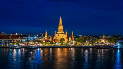 Bangkok wonderful night view of Wat Arun temple beautifully illuminated on the Chao Phraya River with glowing reflections and city lights in the background