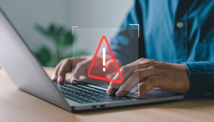 Man working on a laptop with an alert, caution sign on the screen