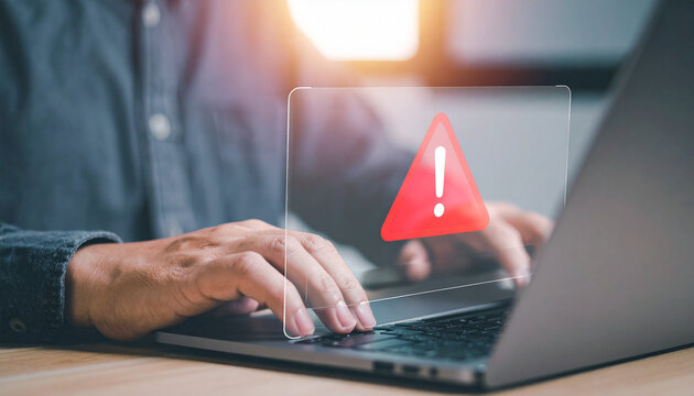 Alert symbol flashing on a laptop screen, indicating a warning message. A person is typing on the laptop. - Powered by Adobe