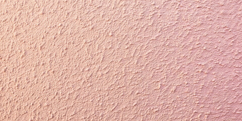 Fototapeta premium A textured wall displays a soft pink hue with uneven surfaces and slight imperfections. The gentle light enhances the warmth, creating a welcoming atmosphere in the room