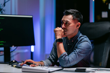 Dedicated adult male software developer focused on intricate coding at night working on technology...