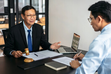 Two men are sitting at a desk with a laptop and a judge's gavel
