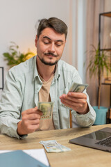 Planning budget. Rich happy man counting money cash using laptop calculate domestic bills at home...