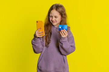Happy preteen child girl kid using credit bank card and smartphone while transferring spending...