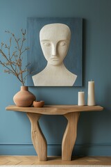 Modern console table with pastel candle, abstract head sculpture, and terracotta vase against blue wall.