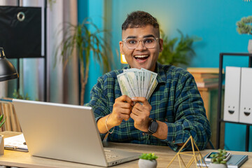 Rich pleased happy Indian man waving money dollar cash banknotes bills like a fan success business...