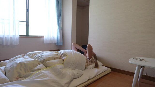 Woman waking up slowly in the japanese style bedroom with white futon mattress