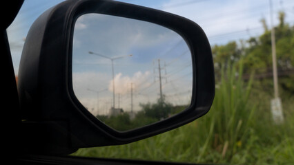 Fototapeta premium Inside view of mirrors wing. Beside car with green grass. Inside mirror wing with top of grass under the sky.