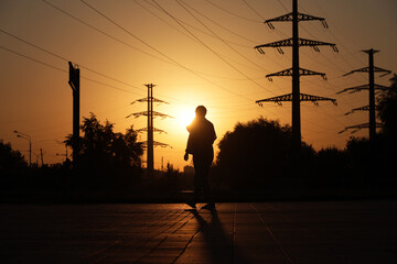 Woman walking on background of high voltage towers with electrical wires. Electricity transmission lines in city at sunset