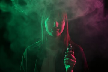 Woman using electronic smoking device in neon lights on black background