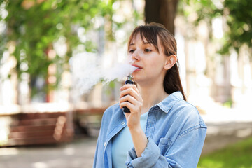 Young woman using electronic smoking device outdoors. Space for text