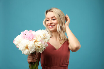 Happy woman with bouquet of beautiful peonies on light blue background