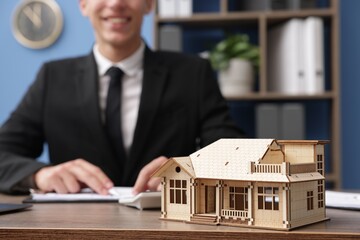 Real estate agent working at desk in office, focus on house model