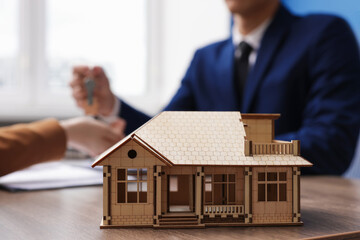 Real estate agent giving key to client at desk in office, focus on house model