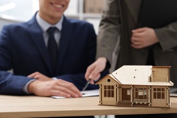 Real estate agent working with client at desk in office, focus on house model