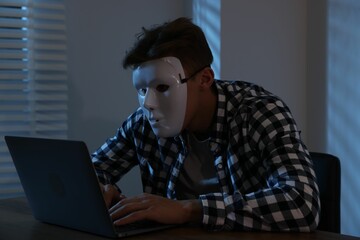 Anonymity. Masked man with laptop at table in dark