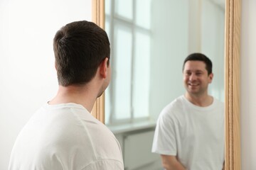 Handsome man looking at himself in mirror indoors