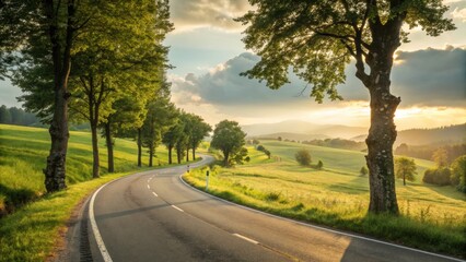 Obraz premium A winding road curves through a picturesque landscape with golden sunlight and green fields, creating a peaceful rural scene.