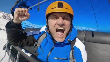 Skier man shows excitement as he rides chair ski lift over a scenic winter mountain landscape with snow-covered slopes and a clear blue sky