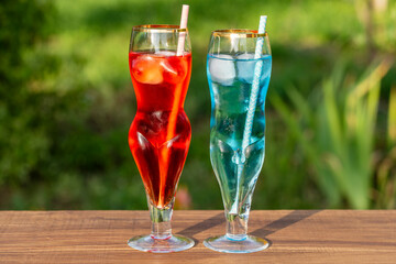 Two artistic glasses shaped like a nude woman and man filled with red and blue alcoholic cocktails...