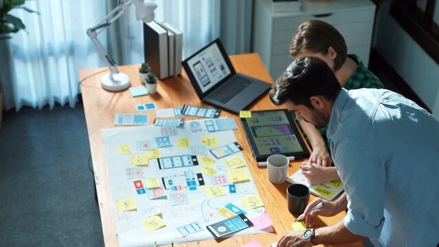 Top view of developer working together to design Ux Ui designing for mobile phone and using laptop programing system or coding engineering prompt while discussing and brainstorming idea. Convocation.
