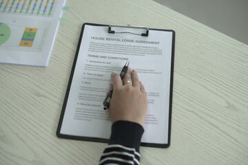 A real estate woman agent is reading and checking paper documents, signing the lease agreement,...