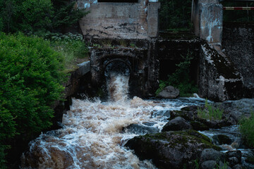 An old dam with a forceful river flowing through on a summer Scandinavian overcast day.
