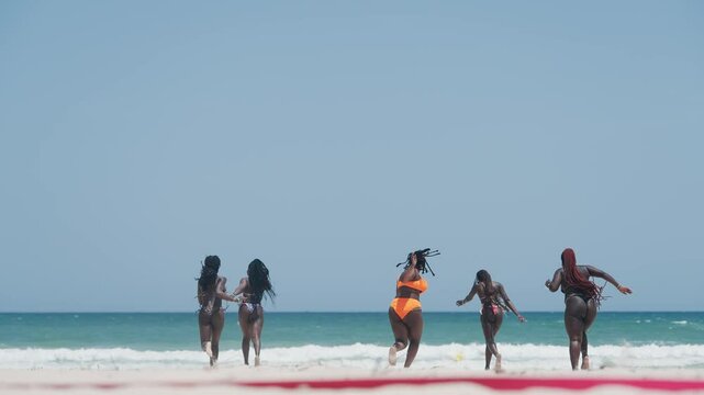 Group of friends running on a sunny beach playing and enjoying summer vacation time together, creating a sense of energy, joy, and friendship, slow motion