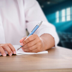 Close up of boy hand writing in notebook at school desk with blurred classroom or university hall...