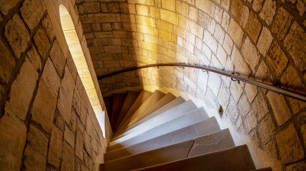Stone spiral staircase with natural light and wooden handrail
