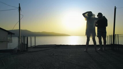 Silhouette of romantic couple standing on balcony enjoying sunset over the sea during summer vacation - Powered by Adobe