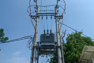 Electric power distribution transformer mounted on a utility pole with high voltage cables,...