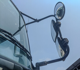 Close-up view of side mirrors on a large truck with clear blue sky background. Safety and...