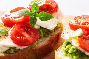 Fresh homemade caprese sandwich with avocado paste, mozzarella cheese, cherry tomatoes, fresh aromatic basil leaves and spicy hot oil macro view. Healthy homemade food concept.