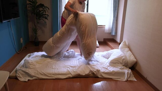 Woman changing bed linens in the japanese style bedroom with white futon mattress