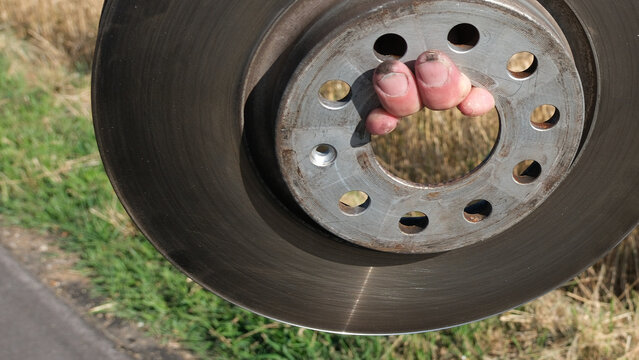 Auto Panne auf dem Lande wegen Problemen mit den Bremsen, defekte Bremsscheibe in der Hand von einem Pannendienst Helfer am Stra&szlig;enrand, KFZ Ersatzteile sind notwendig f&uuml;r eine fachm&auml;nnische Reparatur