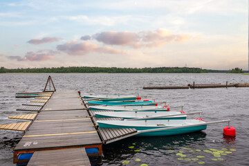 Pier with boats on lake for travel and adventure near green forest under sun set sky
