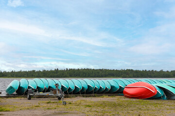 Turquoise boats lined up in order stored on green lakeside shore waiting under blue sky