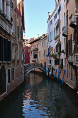 Narrow canal in Venice, Italy with historic buildings on both sides and small arched bridge in the distance; quiet scenic waterway in traditional Venetian architecture setting