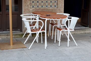 Street view of outdoor cafe setup with round wood table and white chairs on concrete pavement....