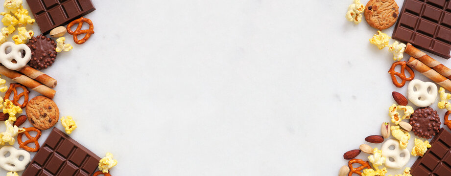 Sweet and salty snacks double border over a white marble banner background. Chocolate, popcorn, pretzels, nuts and cookies. Top view.