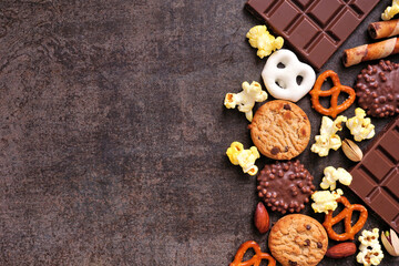 Sweet and salty snacks side border over a dark background. Chocolate, popcorn, pretzels, nuts and cookies. Top view.