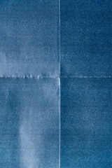 macro photo of blue paper with prominent fold marks forming a cross pattern. The texture is...