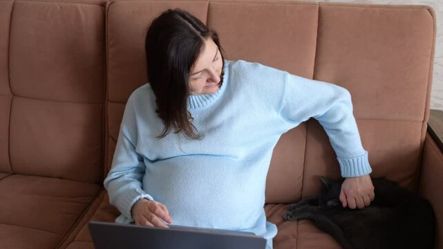 Pregnant woman pets black cat after working on laptop