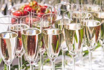 Champagne or sparkling white wine flutes with bubbles on the table during an outdoor party under...