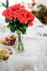 Elegant dining table with a clear vase of red roses, surrounded by glassware and appetizers, creating a festive, romantic atmosphere perfect for celebration or event decoration.