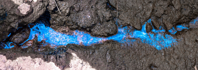 Vibrant blue liquid flowing through cracked soil, creating an abstract pattern